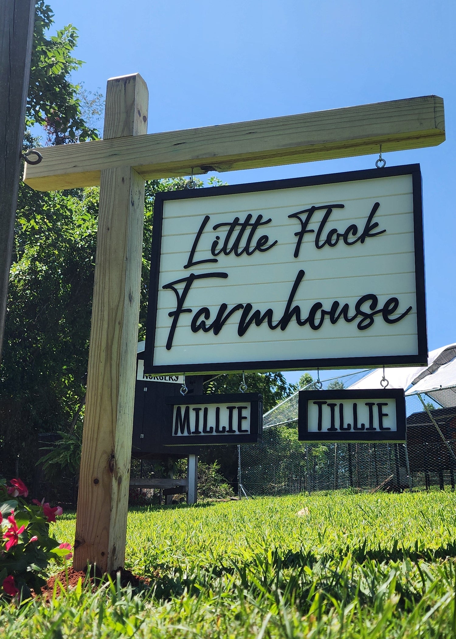 Sign for Little Flock Farmhouse with a wooden frame and greenery in the background