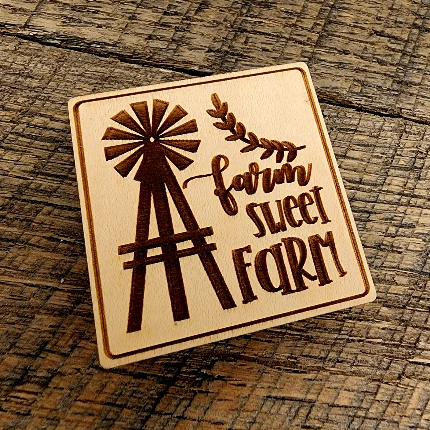 Magnet with "Farm Sweet Farm" printed on it. A windmill design to the left of the lettering and the magnet is tilted left