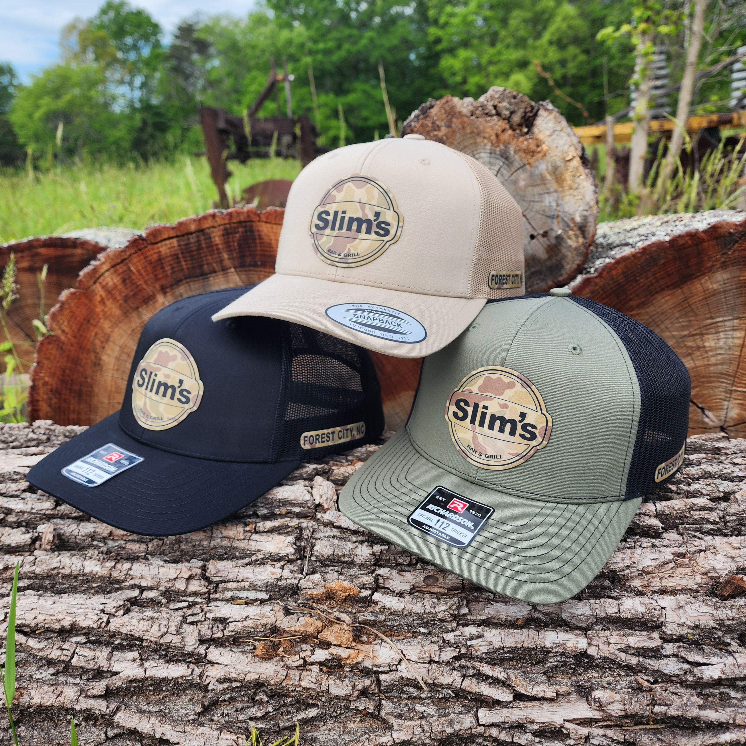 Three caps with Slim's logo on a tree stump outdoors